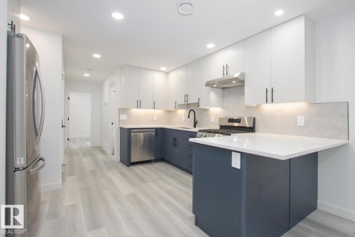 Two tone kitchen featuring dual tone cabinets, stainless steel appliances, a peninsula, decorative backsplash, and light stone countertops - 11016 132 Street, Edmonton, AB - Indoor Photo Showing Kitchen With Stainless Steel Kitchen With Upgraded Kitchen