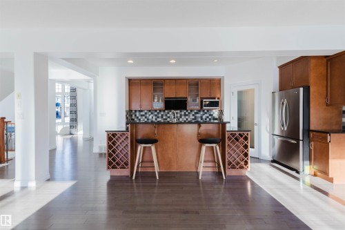 Kitchen featuring stainless steel appliances, glass fronted cabinets, a kitchen bar, dark wood-style flooring, and wood finish cabinetry - 3547 Mclay Crescent, Edmonton, AB - Indoor Photo Showing Kitchen