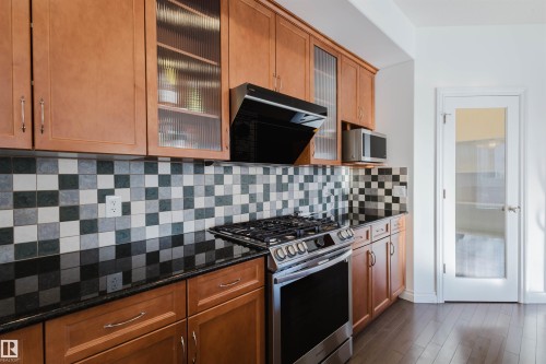 Kitchen with stainless steel appliances, decorative backsplash, exhaust hood, dark stone counters, and wood finish cabinetry - 3547 Mclay Crescent, Edmonton, AB - Indoor Photo Showing Kitchen
