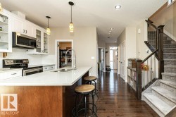 Kitchen featuring stainless steel appliances, glass insert cabinets, decorative light fixtures, a kitchen bar, and dark wood-style flooring - 