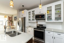 Kitchen featuring stainless steel appliances, white cabinets, pendant lighting, and light stone counters - 