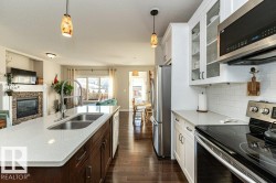 Kitchen with open floor plan, stainless steel appliances, decorative light fixtures, a stone fireplace, and dual tone cabinets - 