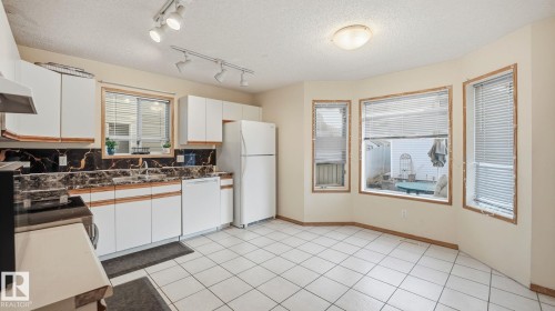 Two tone kitchen featuring white appliances, a textured ceiling, backsplash, light tile patterned floors, and dark countertops - 1509 Jarvis Cr, Edmonton, AB - Indoor Photo Showing Kitchen