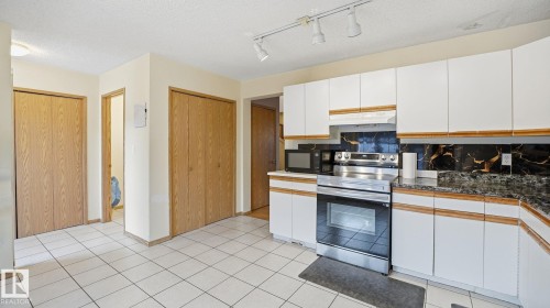 Two tone kitchen with stainless steel electric stove, dark countertops, tasteful backsplash, two tone cabinets, and black microwave - 1509 Jarvis Cr, Edmonton, AB - Indoor Photo Showing Kitchen
