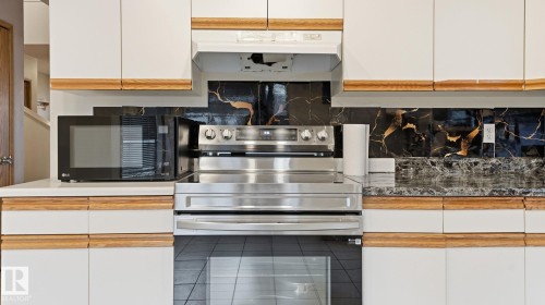 Two tone kitchen with stainless steel electric range oven, black microwave, decorative backsplash, dark countertops, and two tone color scheme - 1509 Jarvis Cr, Edmonton, AB - Indoor Photo Showing Kitchen