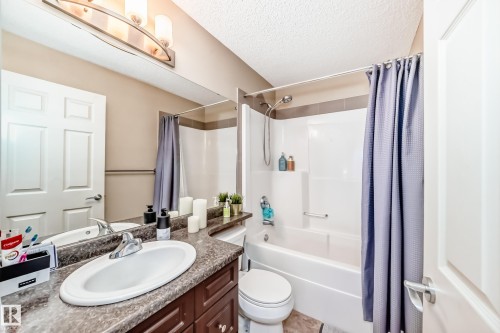 Bathroom featuring vanity, shower / bathtub combination with curtain, and a textured ceiling - 9645 Simpson Place, Edmonton, AB 