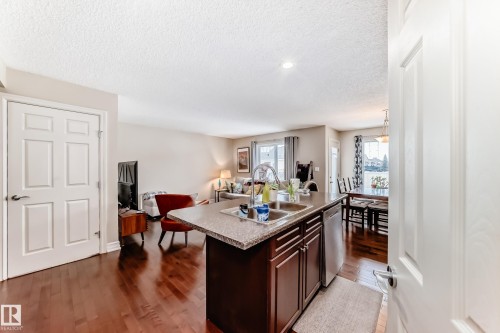 Kitchen with dark wood finish cabinets, a center island with sink, dark wood-type flooring, open floor plan, and stainless steel dishwasher - 9645 Simpson Place, Edmonton, AB 