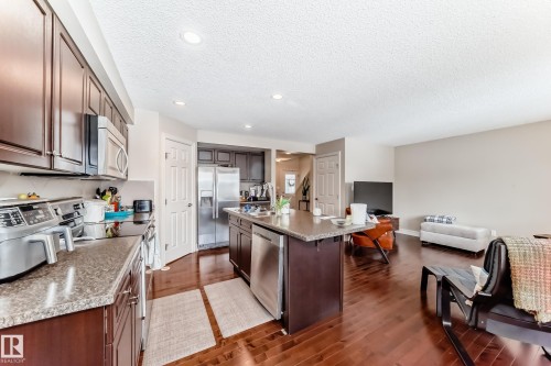 Kitchen with stainless steel appliances, dark wood finish cabinets, dark wood-type flooring, a textured ceiling, and a kitchen island with sink - 9645 Simpson Place, Edmonton, AB 