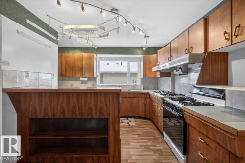Kitchen featuring range with gas cooktop, wood finish cabinets, light wood finished floors, a peninsula, and tasteful backsplash - Edmonton, AB - Indoor Photo Showing Kitchen