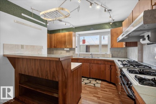 Kitchen with wood finish cabinetry, light wood-type flooring, gas range, light countertops, and decorative backsplash - Edmonton, AB - Indoor Photo Showing Kitchen With Double Sink