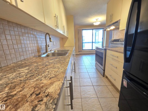 Kitchen with freestanding refrigerator, stainless steel range with electric cooktop, tasteful backsplash, white cabinets, and a textured ceiling - 701 10155 114 Street, Edmonton, AB - Indoor Photo Showing Kitchen With Double Sink