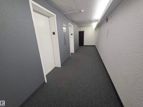 Hallway featuring a textured wall, elevator, dark colored carpet, and a textured ceiling - 701 10155 114 Street, Edmonton, AB - Indoor Photo Showing Other Room