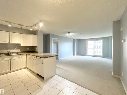 Kitchen with light carpet, white cabinetry, a peninsula, dishwasher, and dark countertops - 1402 10909 103 Avenue, Edmonton, AB - Indoor Photo Showing Kitchen With Double Sink