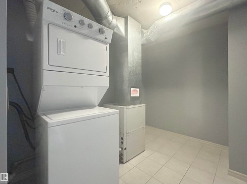 Washroom with stacked washing machine and dryer, light tile patterned flooring, and heating unit - 1402 10909 103 Avenue, Edmonton, AB - Indoor Photo Showing Laundry Room