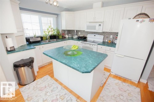Kitchen featuring white appliances, light wood-style flooring, dark countertops, and white cabinets - 17208 106 Street, Edmonton, AB - Indoor Photo Showing Kitchen With Double Sink