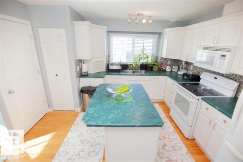 Kitchen featuring white appliances, dark countertops, white cabinets, light wood-type flooring, and a textured ceiling - 17208 106 Street, Edmonton, AB - Indoor Photo Showing Kitchen