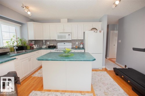 Kitchen featuring white appliances, a kitchen island, white cabinets, dark countertops, and decorative backsplash - 17208 106 Street, Edmonton, AB - Indoor Photo Showing Kitchen With Double Sink