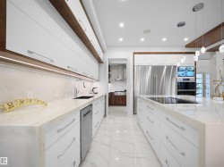 Kitchen with light stone counters, two tone cabinetry, pendant lighting, stainless steel appliances, and modern cabinets - 