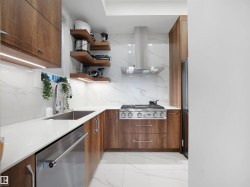 Kitchen featuring exhaust hood, stainless steel appliances, wood finish cabinetry, open shelves, and light marble finish flooring - 