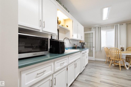 Kitchen featuring stainless steel microwave, white cabinets, open shelves, light wood-style flooring, and dishwasher - 4423 18 Avenue, Edmonton, AB - Indoor Photo Showing Kitchen