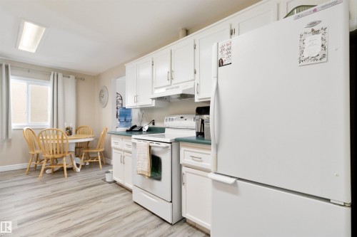 Kitchen with white appliances, white cabinets, light wood finished floors, and dark countertops - 4423 18 Avenue, Edmonton, AB - Indoor Photo Showing Kitchen