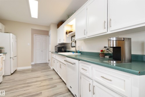 Kitchen with dark countertops, white appliances, white cabinetry, and light wood-type flooring - 4423 18 Avenue, Edmonton, AB - Indoor Photo Showing Kitchen