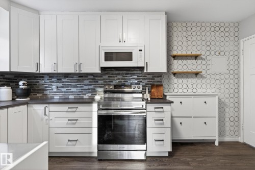 Kitchen featuring stainless steel electric range oven, white microwave, white cabinetry, dark wood-type flooring, and open shelves - 5 Langley Drive, Fort Saskatchewan, AB - Indoor Photo Showing Kitchen