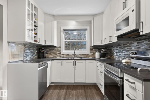 Kitchen featuring stainless steel appliances, dark wood-style flooring, white cabinetry, tasteful backsplash, and glass fronted cabinets - 5 Langley Drive, Fort Saskatchewan, AB - Indoor Photo Showing Kitchen With Upgraded Kitchen