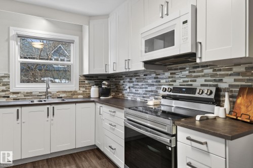 Kitchen featuring stainless steel electric range oven, white microwave, dark countertops, white cabinetry, and dark wood-type flooring - 5 Langley Drive, Fort Saskatchewan, AB - Indoor Photo Showing Kitchen With Double Sink