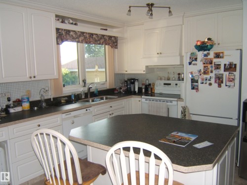Kitchen featuring white appliances, white cabinets, tasteful backsplash, a kitchen bar, and a center island - 4807 54 Avenue, Two Hills, AB - Indoor Photo Showing Kitchen With Double Sink