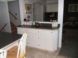 Kitchen featuring dark countertops, white cabinetry, light tile patterned floors, a peninsula, and arched walkways - 