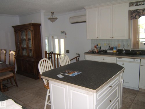 Kitchen with white dishwasher, backsplash, light tile patterned floors, crown molding, and dark countertops - 4807 54 Avenue, Two Hills, AB - Indoor Photo Showing Kitchen