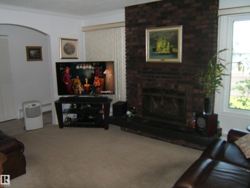 Living room featuring ornamental molding, a brick fireplace, carpet, and a textured ceiling - 4807 54 Avenue, Two Hills, AB - Indoor Photo Showing Living Room With Fireplace