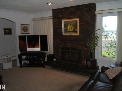 Carpeted living room featuring crown molding, a textured ceiling, and a brick fireplace - 4807 54 Avenue, Two Hills, AB - Indoor Photo Showing Living Room With Fireplace