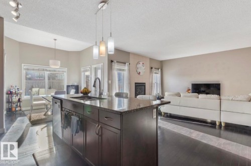 Kitchen featuring light stone countertops, dark wood-style flooring, dark wood finish cabinetry, a textured ceiling, and a kitchen island with sink - 21703 86 Avenue, Edmonton, AB - Indoor Photo Showing Kitchen With Upgraded Kitchen