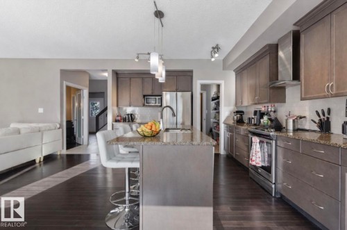 Kitchen with stainless steel appliances, dark wood finish cabinetry, a breakfast bar area, tasteful backsplash, and a textured ceiling - 21703 86 Avenue, Edmonton, AB - Indoor Photo Showing Kitchen With Upgraded Kitchen