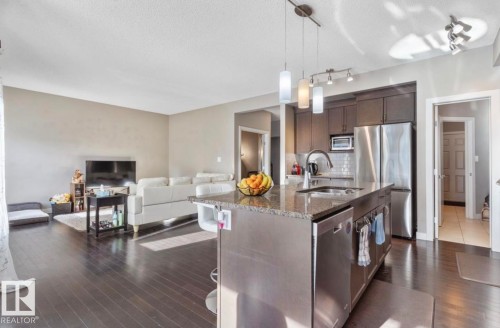 Kitchen with dark wood finish cabinets, dark stone counters, open floor plan, decorative light fixtures, and stainless steel appliances - 21703 86 Avenue, Edmonton, AB - Indoor Photo Showing Kitchen With Upgraded Kitchen