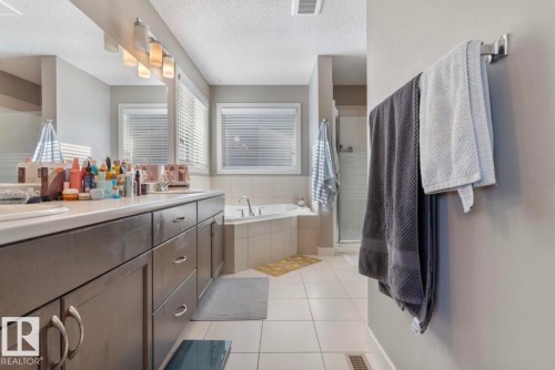 Full bath with double vanity, a stall shower, light tile patterned floors, a textured ceiling, and a garden tub - 21703 86 Avenue, Edmonton, AB - Indoor Photo Showing Bathroom