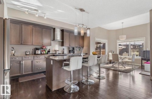 Kitchen featuring hanging light fixtures, a breakfast bar area, dark stone countertops, tasteful backsplash, and dark wood finish cabinetry - 21703 86 Avenue, Edmonton, AB - Indoor Photo Showing Kitchen With Upgraded Kitchen