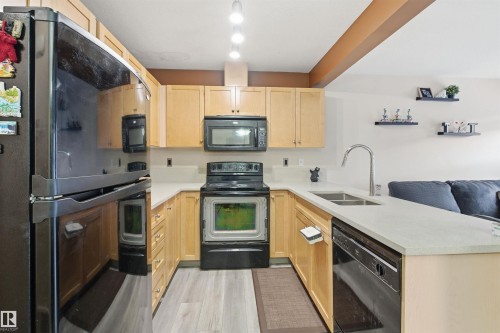 Kitchen featuring black appliances, light wood finish cabinetry, a peninsula, and open floor plan - 8 230 Edwards Drive, Edmonton, AB - Indoor Photo Showing Kitchen With Double Sink