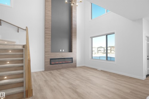 Unfurnished living room featuring a high ceiling, light wood-type flooring, hanging lights, and a fireplace - 6228 29 Avenue, Edmonton, AB - Indoor With Fireplace