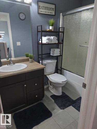 Bathroom featuring vanity, shower / bath combination with glass door, and light tile patterned flooring - 4 4350 23 Street, Edmonton, AB - Indoor Photo Showing Bathroom