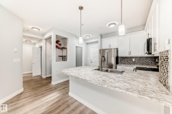 Kitchen with a peninsula, white cabinetry, pendant lighting, stainless steel fridge with ice dispenser, and backsplash - 