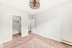 Unfurnished bedroom featuring baseboard heating, a walk in closet, and light carpet - 