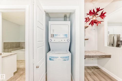 Laundry area featuring stacked washer / drying machine and light wood-style floors - 201 2588 Anderson Way, Edmonton, AB - Indoor Photo Showing Laundry Room