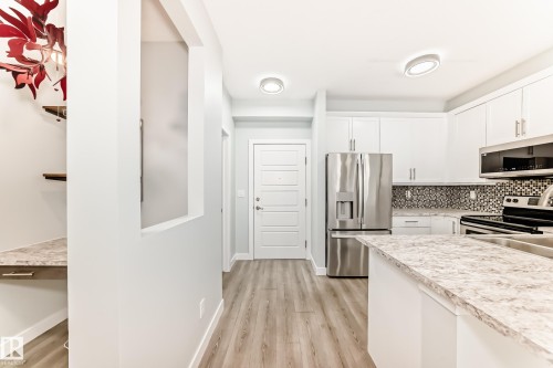 Kitchen with light countertops, stainless steel appliances, light wood-style flooring, backsplash, and white cabinets - 201 2588 Anderson Way, Edmonton, AB - Indoor Photo Showing Kitchen
