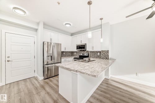Kitchen featuring light countertops, stainless steel appliances, hanging light fixtures, white cabinetry, and a breakfast bar area - 201 2588 Anderson Way, Edmonton, AB - Indoor Photo Showing Kitchen With Upgraded Kitchen
