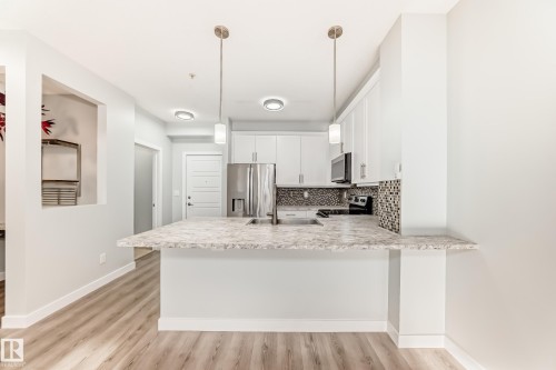 Kitchen featuring tasteful backsplash, white cabinetry, a peninsula, stainless steel appliances, and light wood-style floors - 201 2588 Anderson Way, Edmonton, AB - Indoor Photo Showing Kitchen With Upgraded Kitchen