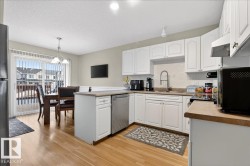 Kitchen with a peninsula, backsplash, white cabinets, black appliances, and light wood-style flooring - 