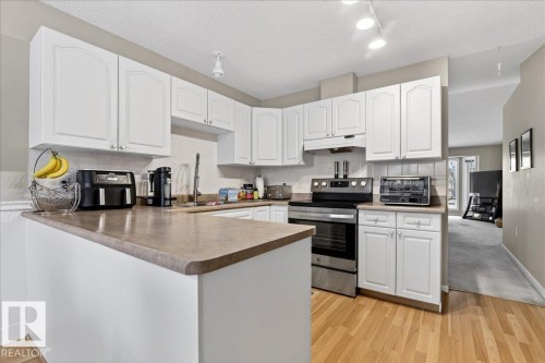Kitchen featuring stainless steel range with electric cooktop, white cabinetry, a peninsula, a textured ceiling, and tasteful backsplash - 13217 155 Avenue Nw, Edmonton, AB - Indoor Photo Showing Kitchen With Double Sink